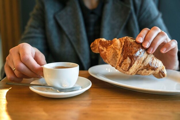 Garota bebe café quente e segura um croissant sentado em um café
