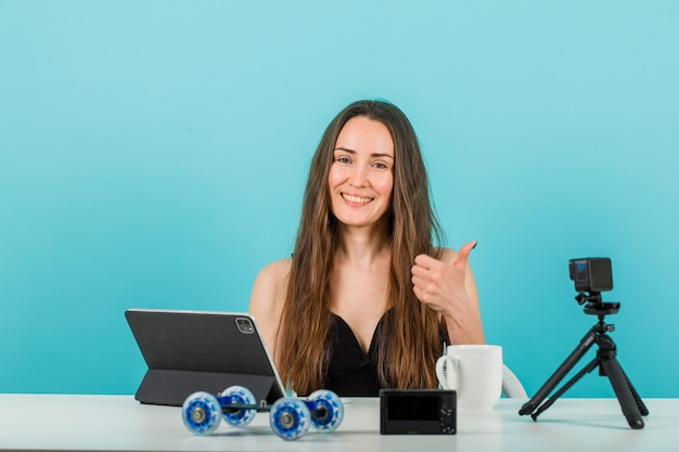 Foto garota blogueira sorridente está olhando para a câmera apontando para a direita com o polegar no fundo azul