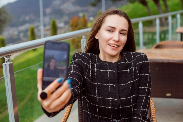 Garota blogueira sorridente está olhando para a câmera traseira do smartphone no fundo da visão da natureza