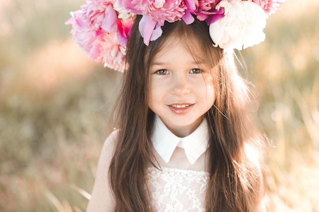 Garota bonita e bonita usando guirlanda floral de flores de peônia posando no campo ao ar livre