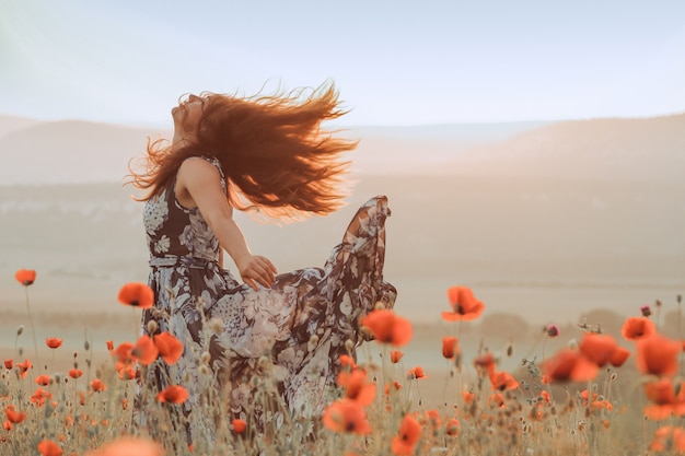 Garota bonita em um campo de papoulas ao pôr do sol. conceito de liberdade