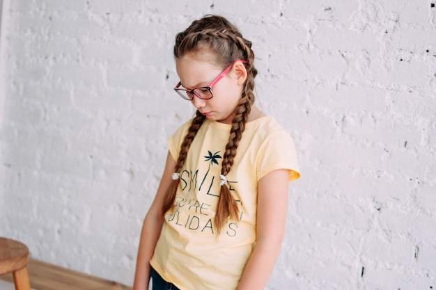 Garota bonita tweens triste em copos com cabelo comprido, isolado na parede de tijolo branco