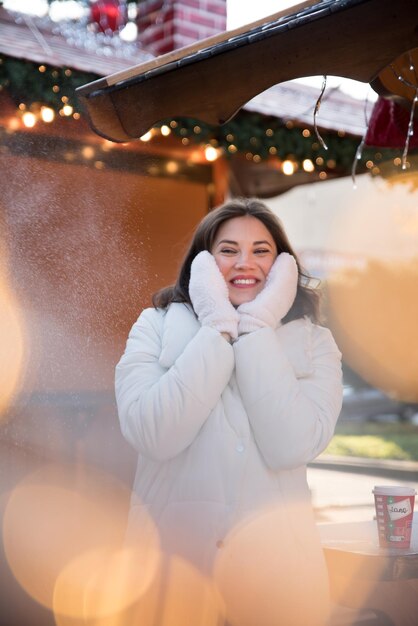 Garota bonita vestida com uma jaqueta branca e um chapéu branco a garota sorri xícara de café na mão casa de verão de madeira garota se alegra emoções