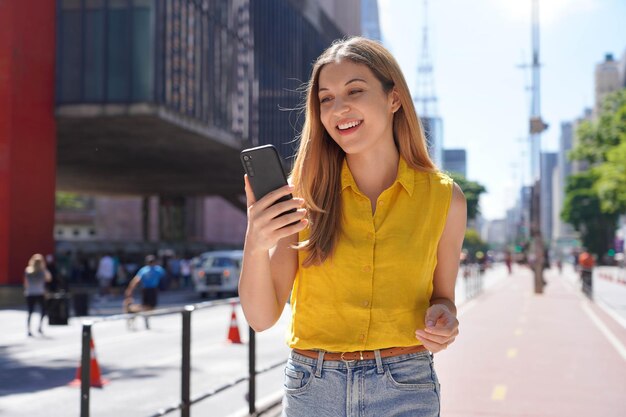 Garota brasileira usando smartphone em dia ensolarado na Avenida Paulista São Paulo Brasil