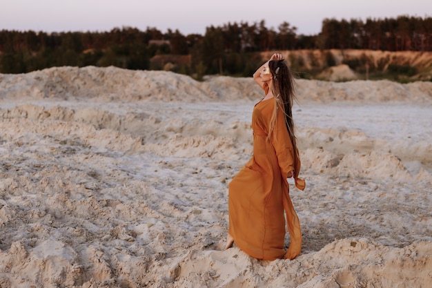 Garota bronzeada em um penioire nas areias ao pôr do sol no verão