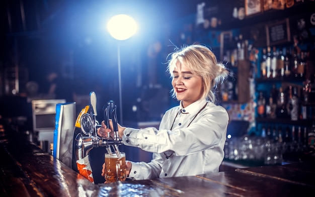 Garota carismática barman derramando bebida alcoólica fresca nos copos em pé perto do balcão do bar na boate