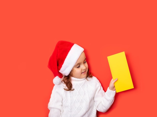 Garota caucasiana bonita com chapéu de papai noel vermelho olha no certificado ou cartão de saudação vazio espaço de cópia para design ou texto banner modelo de maquete de natal