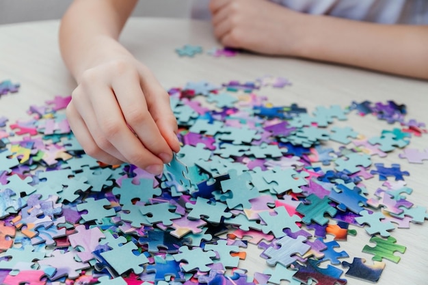 Garota caucasiana coleta quebra-cabeças na mesa A mão da garota segura uma peça de quebra-cabeça fechada