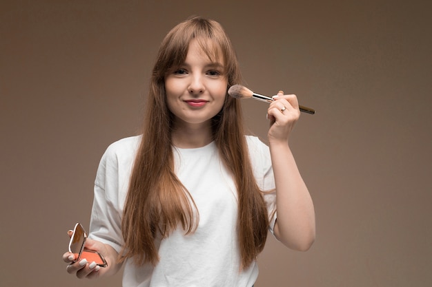 Garota caucasiana em uma camiseta branca com pincel de maquiagem em uma parede escura