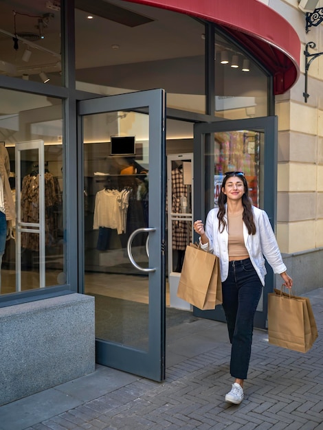 Foto garota caucasiana sorridente feliz saindo de uma loja com sacolas de compras dia de compras pechinchas sexta-feira negra