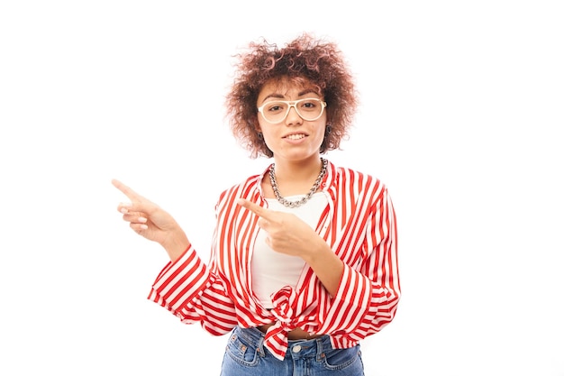 Garota cazaque positiva com penteado afro aponta o dedo indicador no espaço de cópia isolado no fundo branco do estúdio