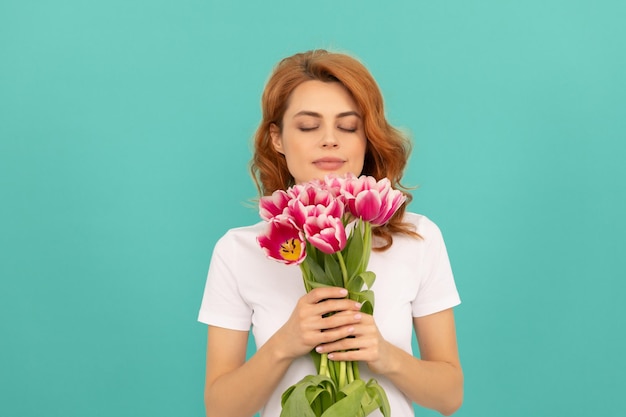 Garota cheira buquê de flores de tulipa em fundo azul