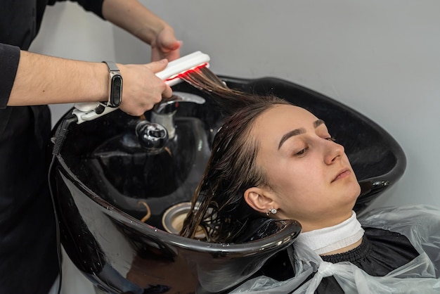 Garota cliente muito elegante sorri em um salão de beleza quando sua cabeça é lavada por um mestre profissional Conceito de mulher feliz em tratamentos de beleza