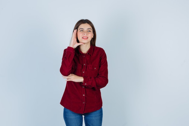 garota com blusa cor de vinho segurando a mão na cabeça enquanto sorri e parece jovial