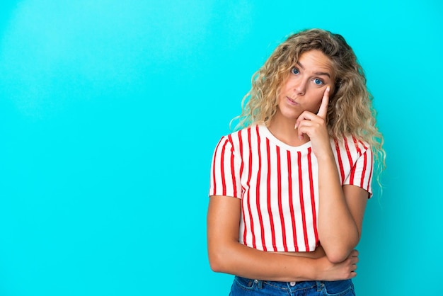 Garota com cabelo encaracolado, isolada em fundo azul, pensando em uma ideia