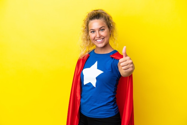 Garota com cabelo encaracolado isolado em fundo amarelo em traje de super-herói com o polegar para cima