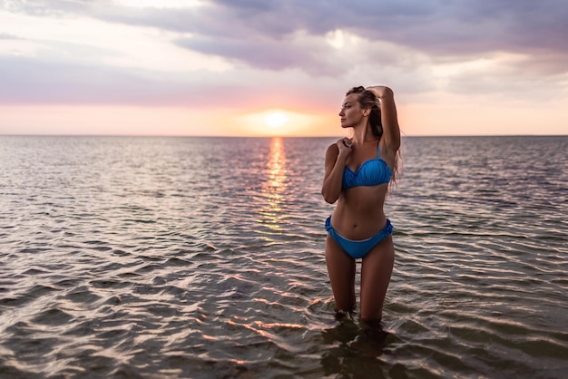 Garota com cabelo loiro em um maiô posando contra o pano de fundo do pôr do sol no estuário curtindo a natureza ao seu redor