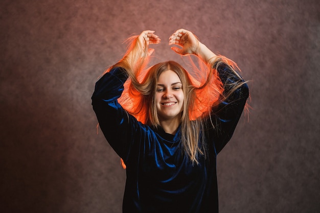 Garota com cabelo loiro, emocionalmente posando em um fundo cinza. O cabelo dela está iluminado em vermelho