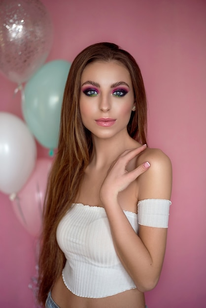 Garota com cabelo longo cacheado, posando em um fundo rosa. Retrato de uma jovem feliz e sorridente.