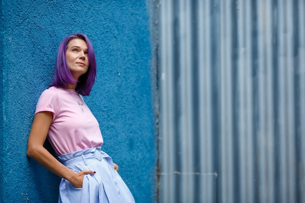 Garota com cabelo roxo fica contra a parede azul