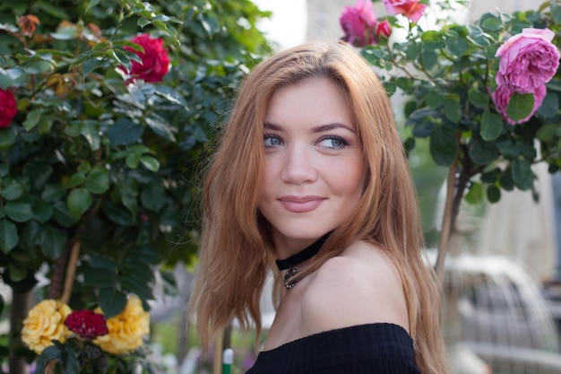 Garota com cabelo vermelho em um vestido preto. arbustos de rosas.