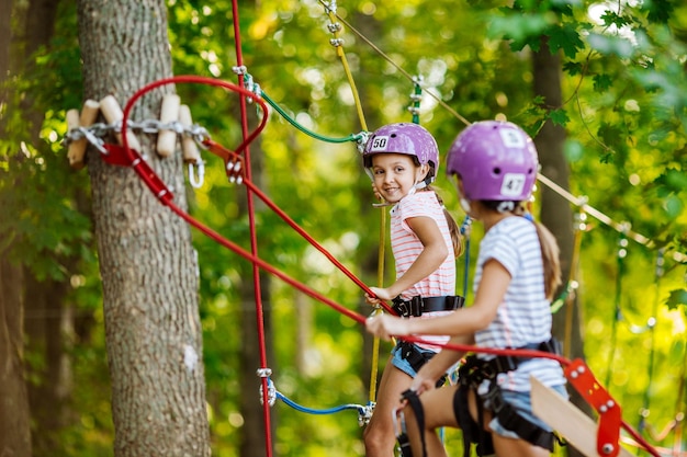 Garota com equipamento de escalada em um parque de aventura está envolvida em escalada ou passa por obstáculos na estrada de corda