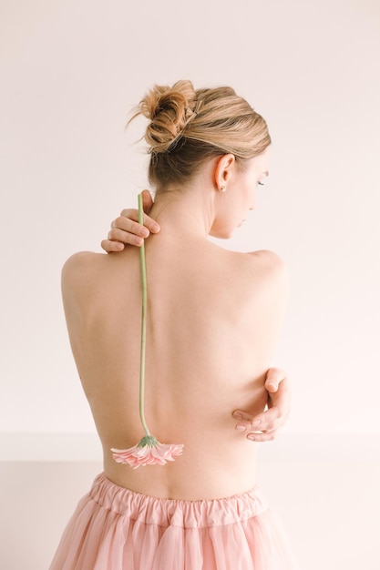 Garota com flor gerbera nua de cabelo amarrado em um fundo branco de rabo de cavalo