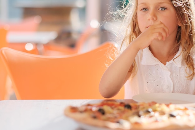 Garota com fome comendo pizza no terraço do café em dia ensolarado fora do espaço de cópia do restaurante