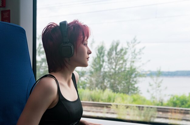 Garota com fones de ouvido anda em um trem suburbano em movimento e olha pela janela