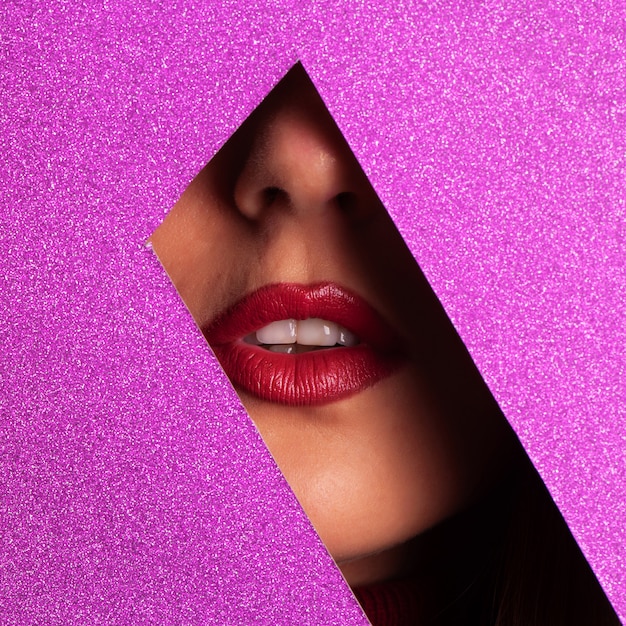 Garota com maquiagem brilhante, batom vermelho, olhando através do buraco no papel violeta