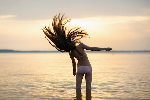 Garota com o cabelo solto no mar durante o pôr do sol