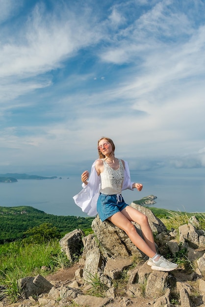 Garota com roupas de verão no topo da montanha perto do mar