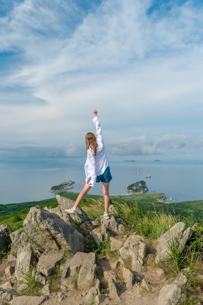 Garota com roupas de verão no topo da montanha perto do mar