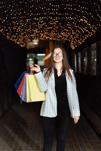 Garota com sacolas de compras caminha pela cidade à noite Quadro vertical