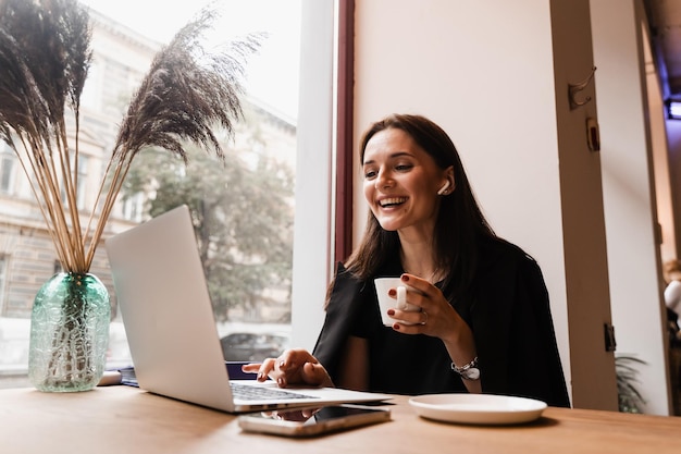 Garota com sorriso de laptop ri e discute situações engraçadas no trabalho com colegas Reunião de vídeo com amigos e colegas e se diverte on-line remotamente após projeto bem-sucedido