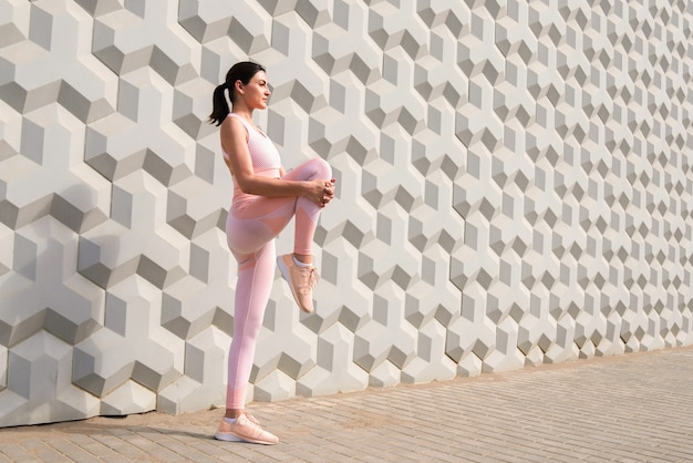 Garota com um agasalho de treino rosa se preparando para um treino alonga os músculos