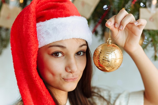 Foto garota com um chapéu de natal com uma árvore de natal de brinquedo na mão.