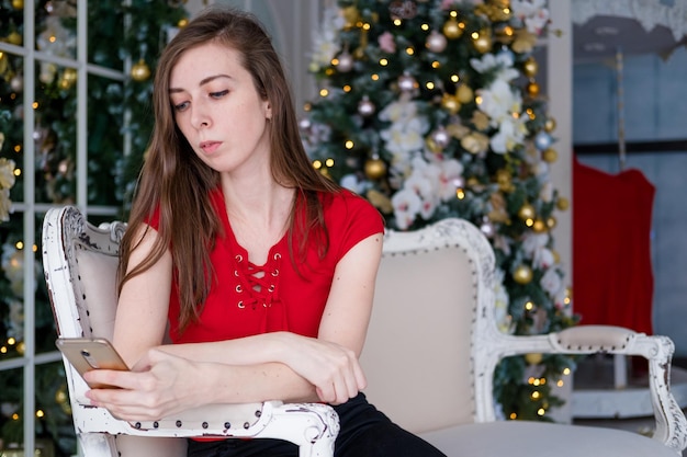 Garota com um telefone no fundo de uma árvore de Natal Trabalho freelance via telefone