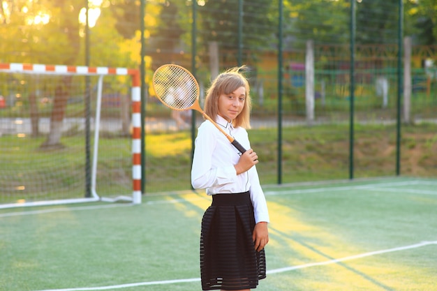 Garota com um uniforme escolar com uma raquete nas mãos no campo de futebol.