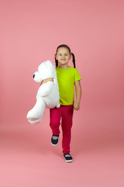 garota com uma camiseta verde clara e calça vermelha marcha com um ursinho de pelúcia branco