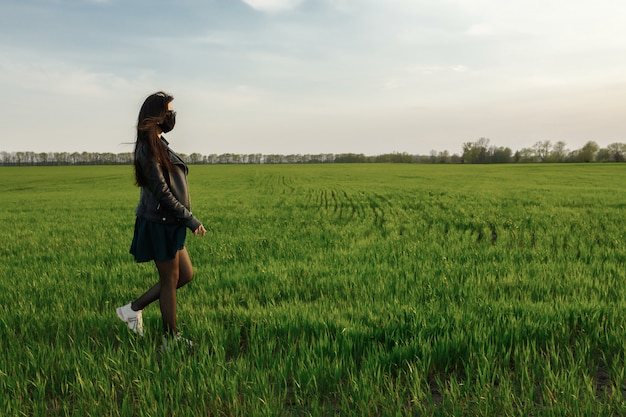 garota com uma máscara médica corre ou caminha sobre um campo verde. Quarentena primavera verão. COVID 19.