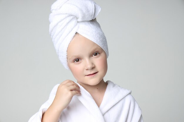 Garota com uma túnica branca e uma toalha na cabeça depois do banho e lavar o cabelo.