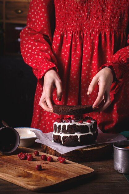 Garota com vestido vintage vermelho preparando um bolo de chocolate com cerejas