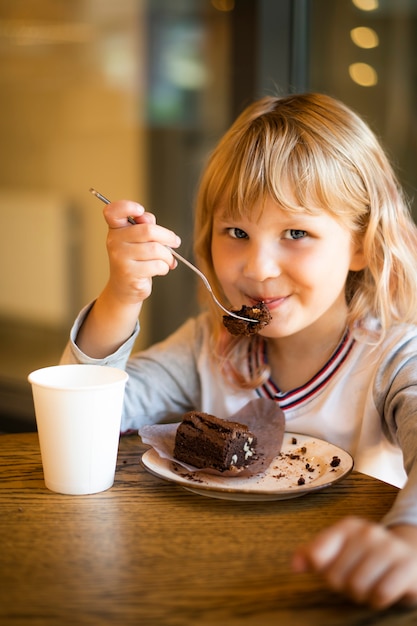 Garota come bolo de chocolate como sobremesa em um café