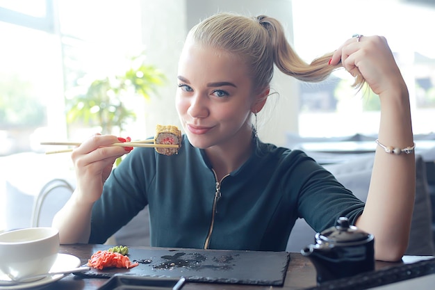 garota come sushi e rola em um restaurante / culinária oriental, comida japonesa, jovem modelo em um restaurante