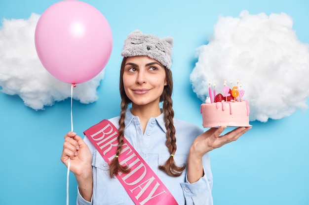 garota comemora aniversário gosta de atmosfera festiva usa camisa causal vendada poses com bolo delicioso e balão inflado isolado no azul