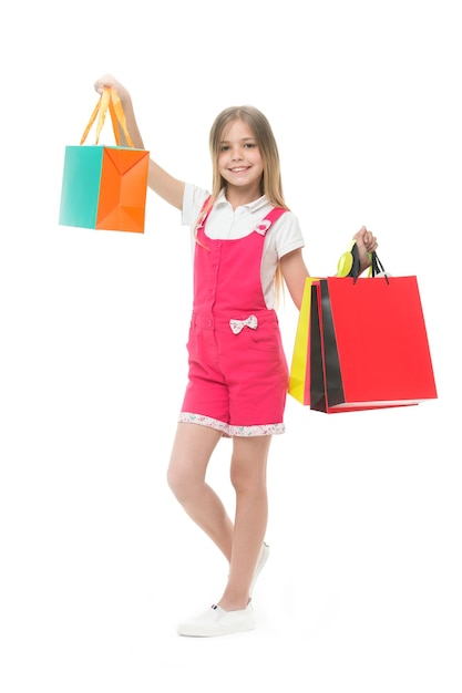 Garota compradora sorri com sacos isolados em branco Criança feliz segura sacolas de compras Pequeno viciado em compras sorrindo com presentes Tempo para presentes Compras e venda