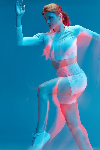 Garota correndo em uniforme esportivo branco em modelo esportivo isolado de fundo azul em estúdio com luz