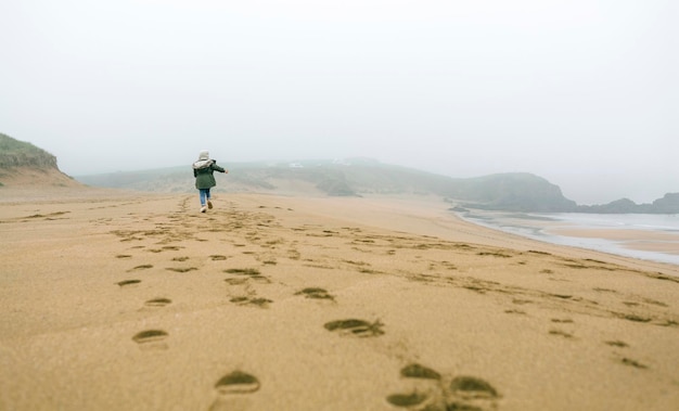 Garota correndo na praia em um dia nublado de inverno