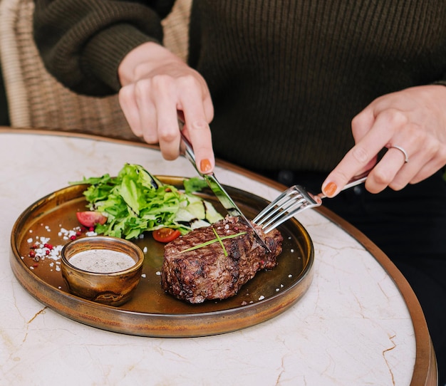 Garota corta um bife frito em um restaurante no terraço